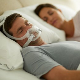 Man sleeping with CPAP mask in bed holding woman's hand