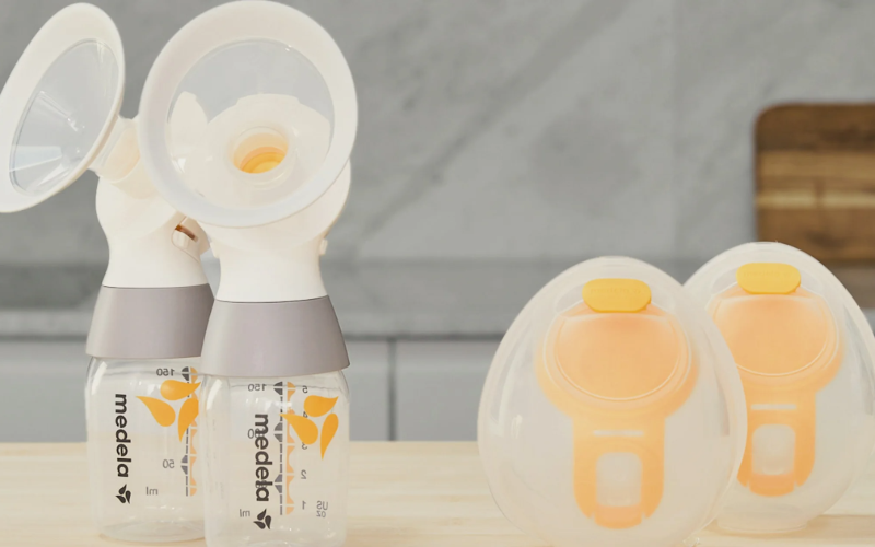 Two Medela breast pump bottles with attached breast shields and two hands-free collection cups on a wooden counter, representing essential maternity supplies for birthing parents.