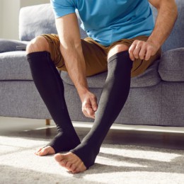Person putting on open toe compression socks sitton on a couch
