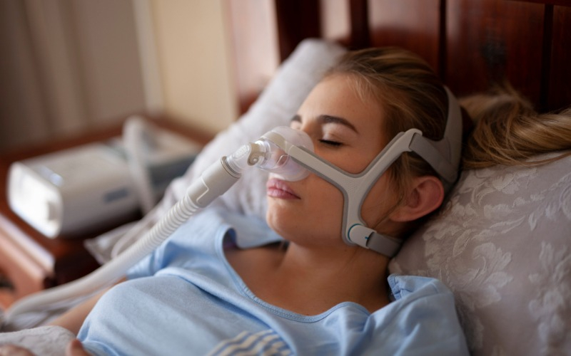 A calm woman sleeping with a CPAP mask, showcasing comfortable sleep apnea therapy.