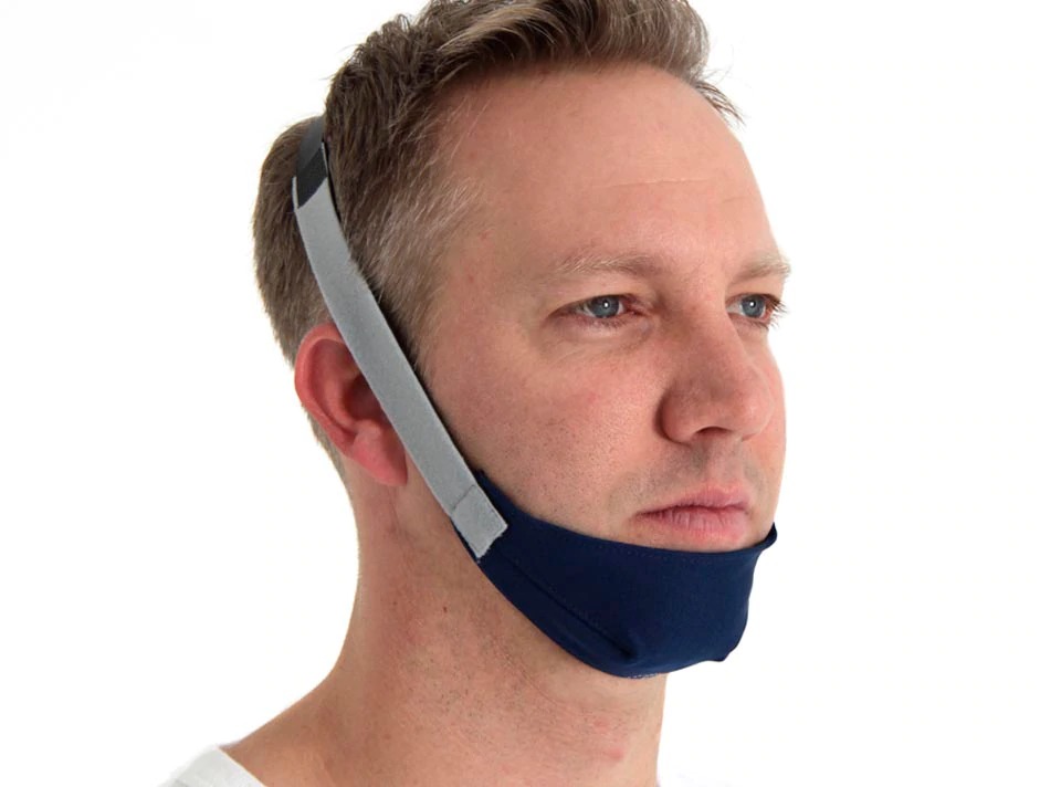 Man wearing a dark blue and grey ResMed CPAP chin strap restraint to prevent mouth breathing during sleep therapy. Product Image