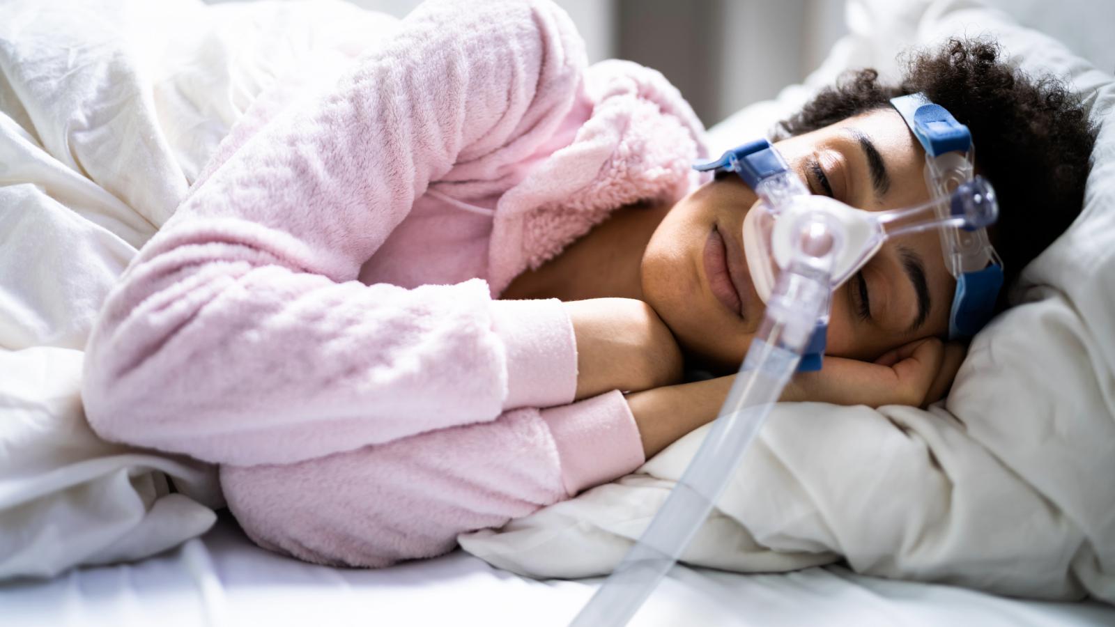 Woman sleeping on her side with a CPAP mask, with hands under her face