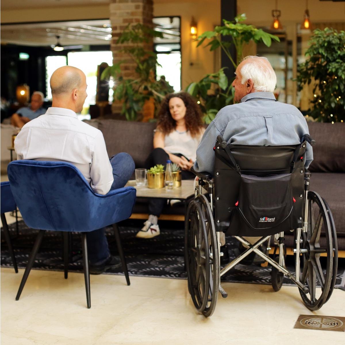 Person sitting in a wheelchair using the Sitnstand wheelchair lift chair in a group