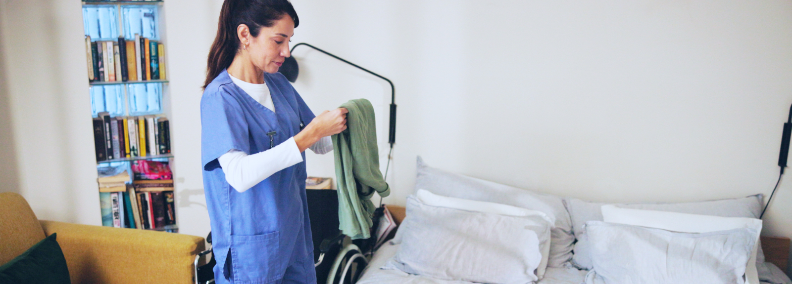 Nurse in home, folding laundry with a wheelchair in the background