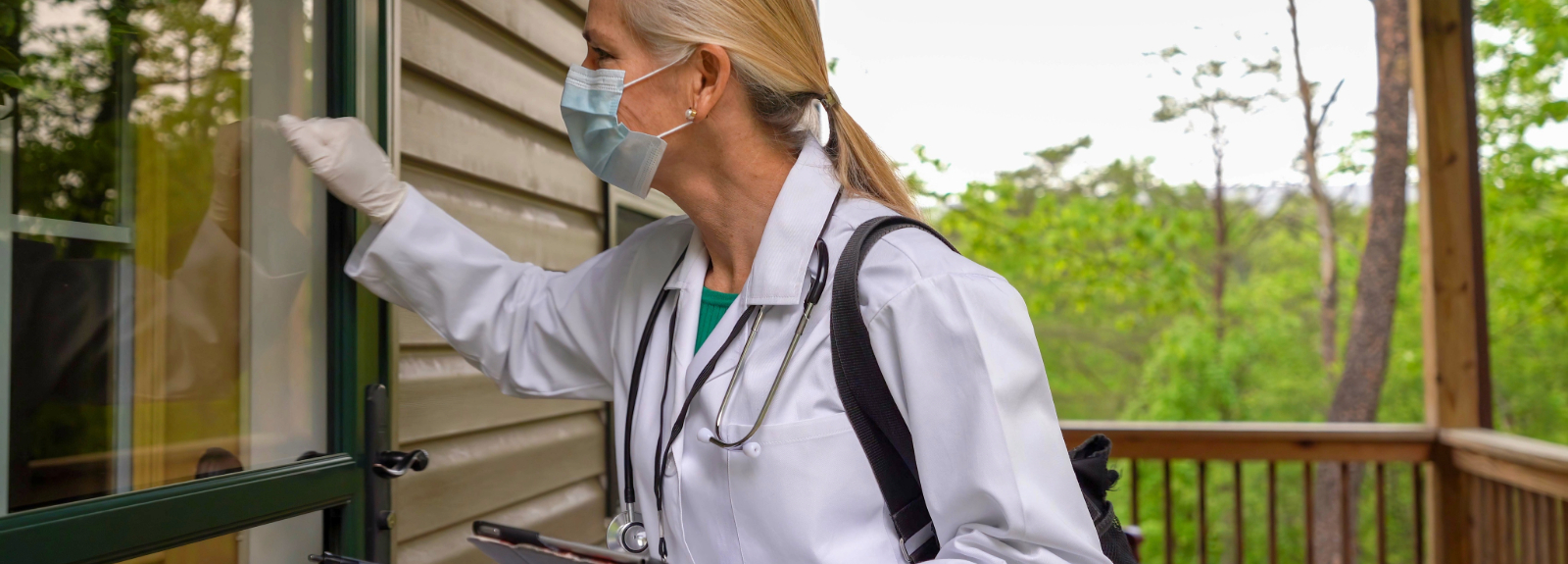 Nurse wearing mask, holding a clipboard knocks at the front door 