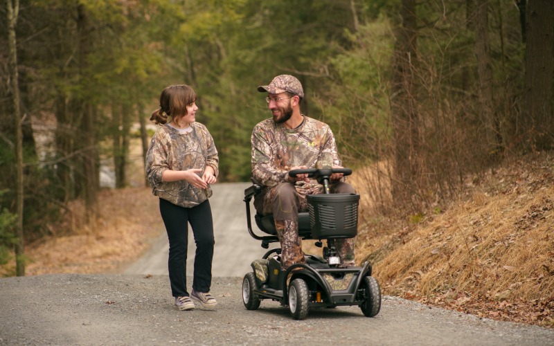Man riding mobility scooter with daughter in the woods