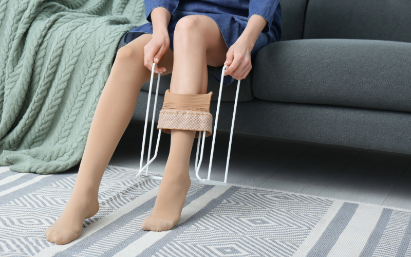 Person sitting on couch putting on compression socks with a donner device