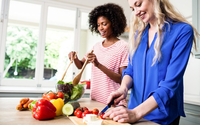 Two women cutting vegetables making a salad