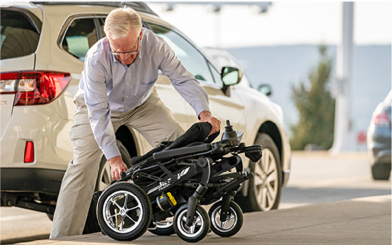 Man folding up Pride Jazzy Passport portable power wheelchair